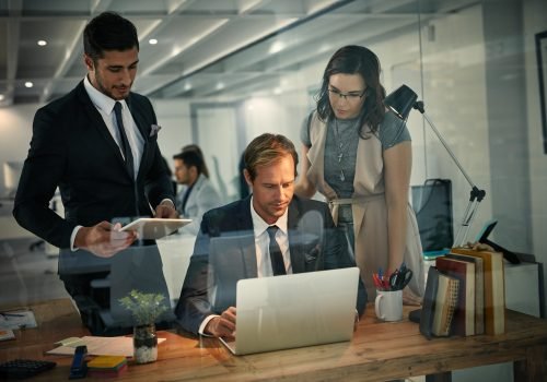 Shot of a team of colleagues using a laptop together on a night shift at work.